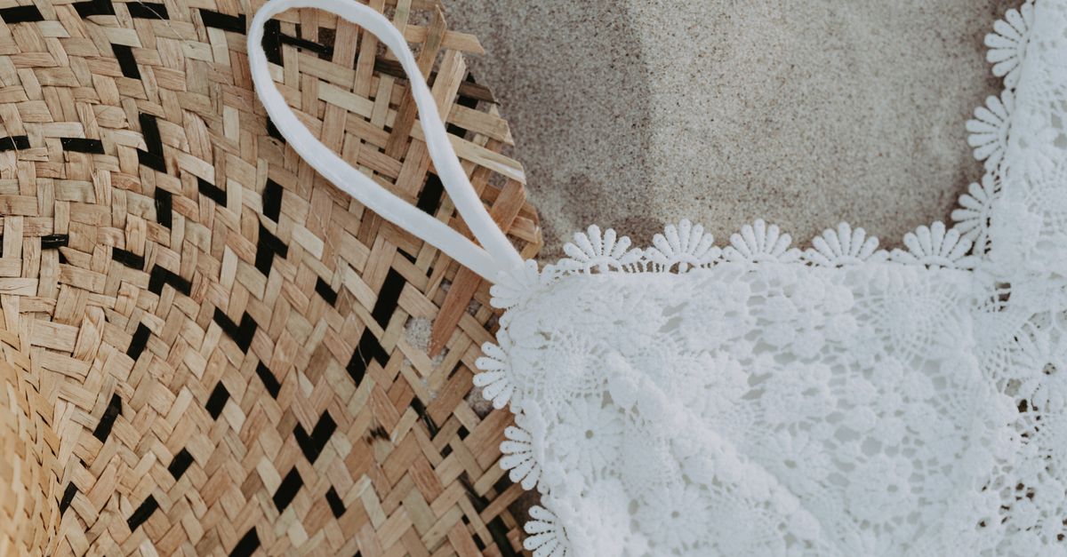 White swim top and a straw beach bag on sand